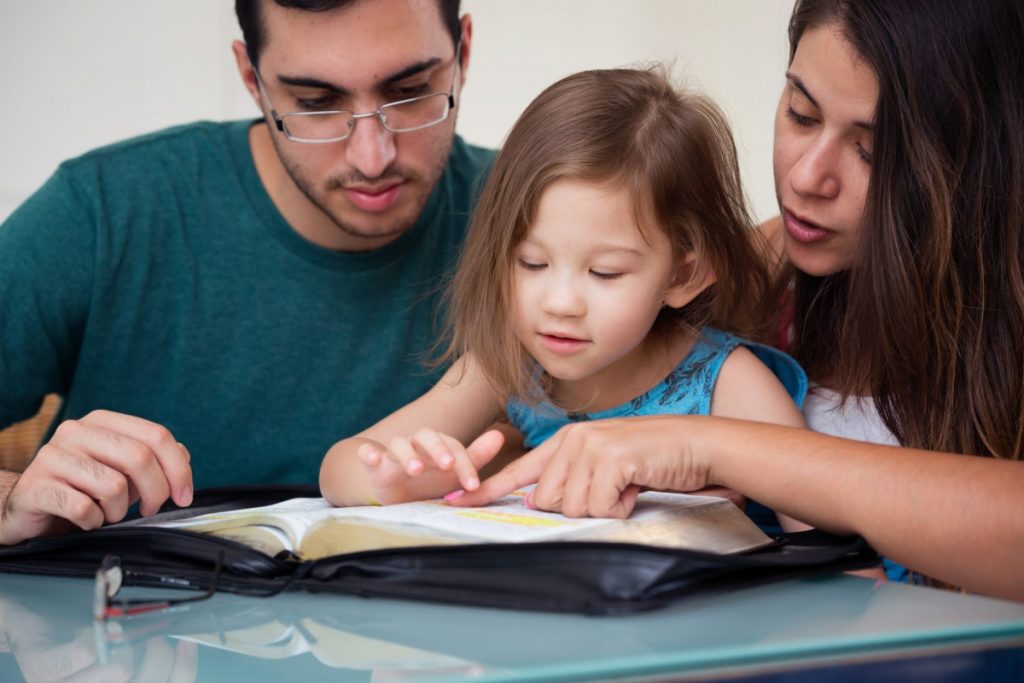 Junge Familie, Eltern lesen gemeinsam mit Grundschulkind.